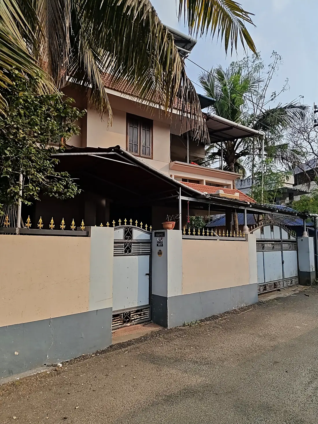 The front of Gowreesam Homestay behind its gate, with a tiled roof and coconut palms